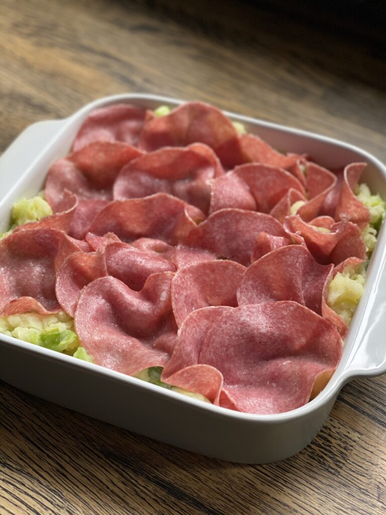 Prei ovenschotel plakjes salami verdelen over aardappelpuree