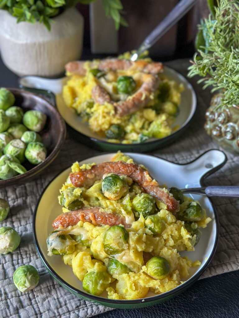 spruitjes ovenschotel met aardappelpuree en chipolata worstjes geserveerd op rond bord