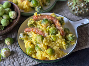 Spruitjes ovenschotel met romige aardappelpuree, chipolata worstjes en een goudbruin laagje gesmolten kaas