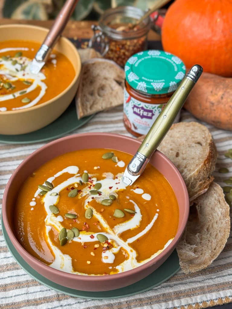 pompoensoep met zoete aardappel en harissa in een kom met een swirl kokosmelk