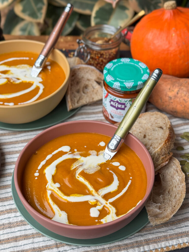 romige pompoensoep met zoete aardappel en harissa in roze kom