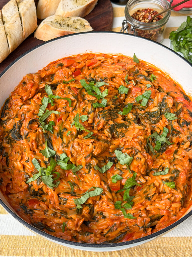 orzo in romige tomatensaus geserveerd in pan met verse basilicum