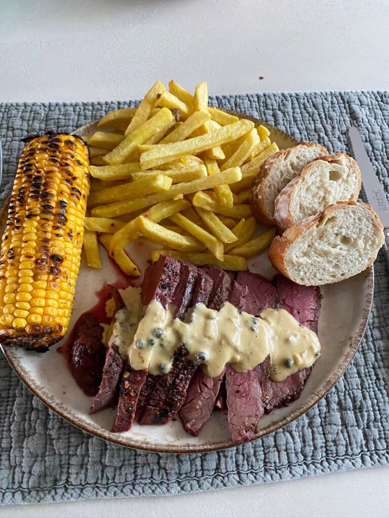een bord met frietjes, steak, mais en stokbrood