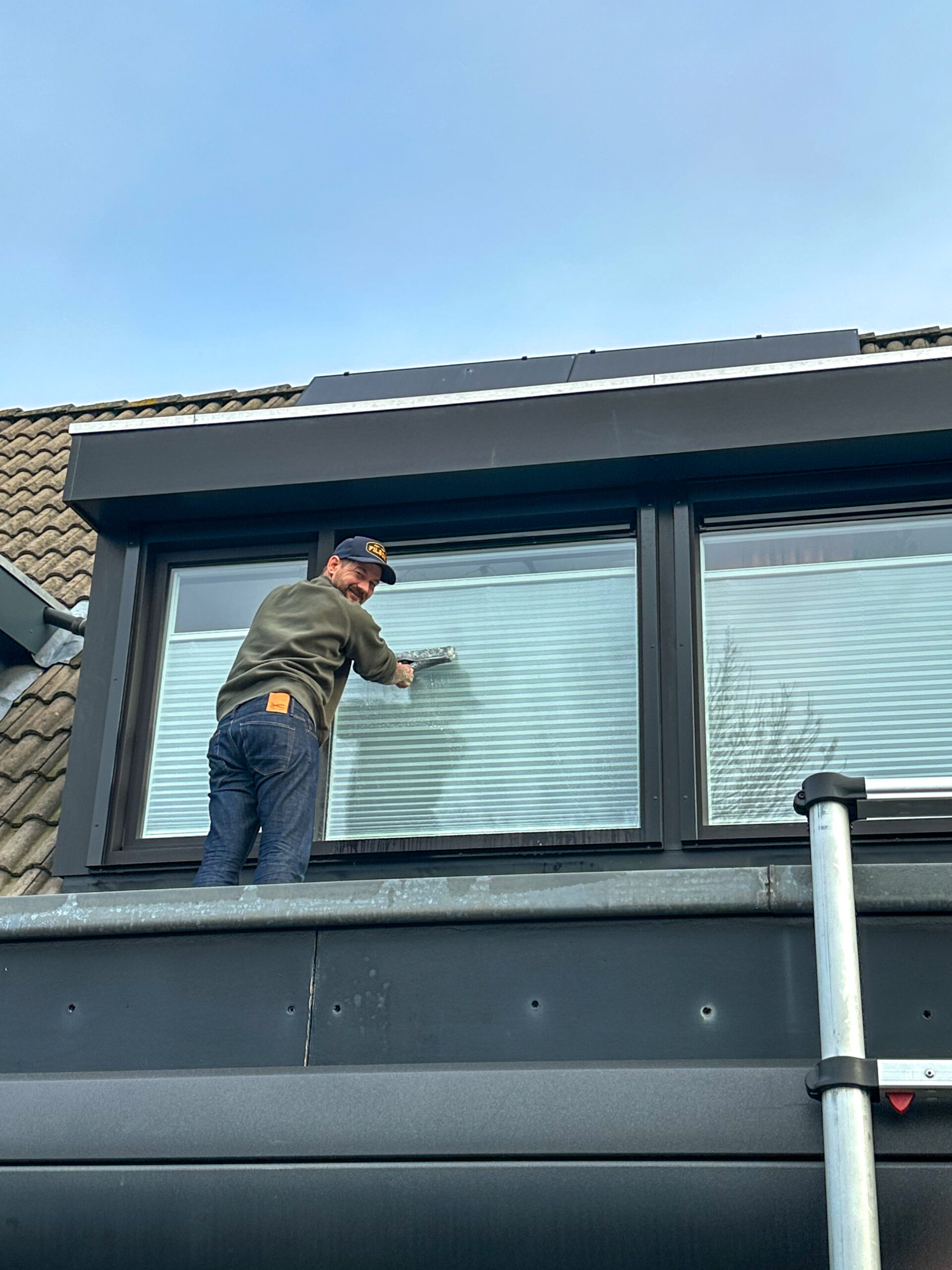 Jan Willem die de bovenramen van het huis wast.