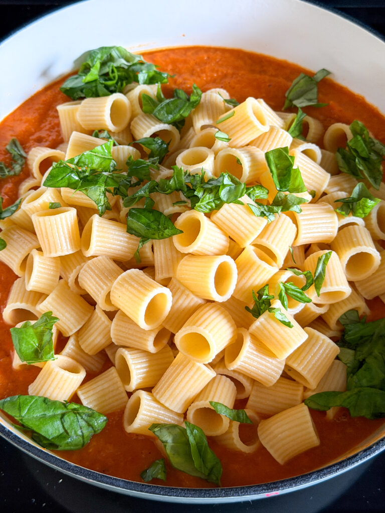 Gekookte pasta en verse basilicum toevoegen aan pastasaus met pompoen