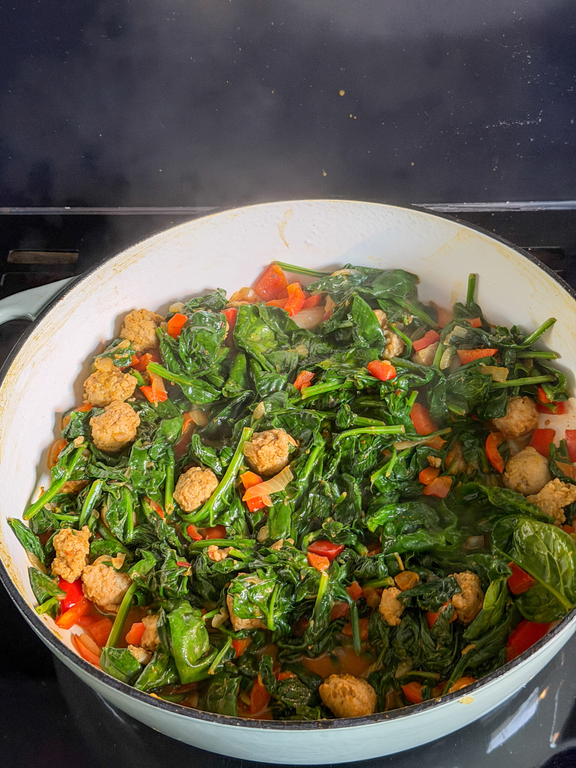 Spinazie toevoegen aan de pan met paprika en worst
