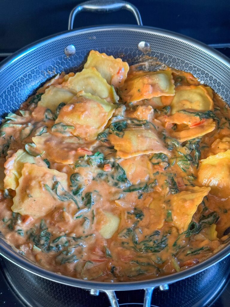 Ravioli mengen door de romige tomatensaus met spinazie