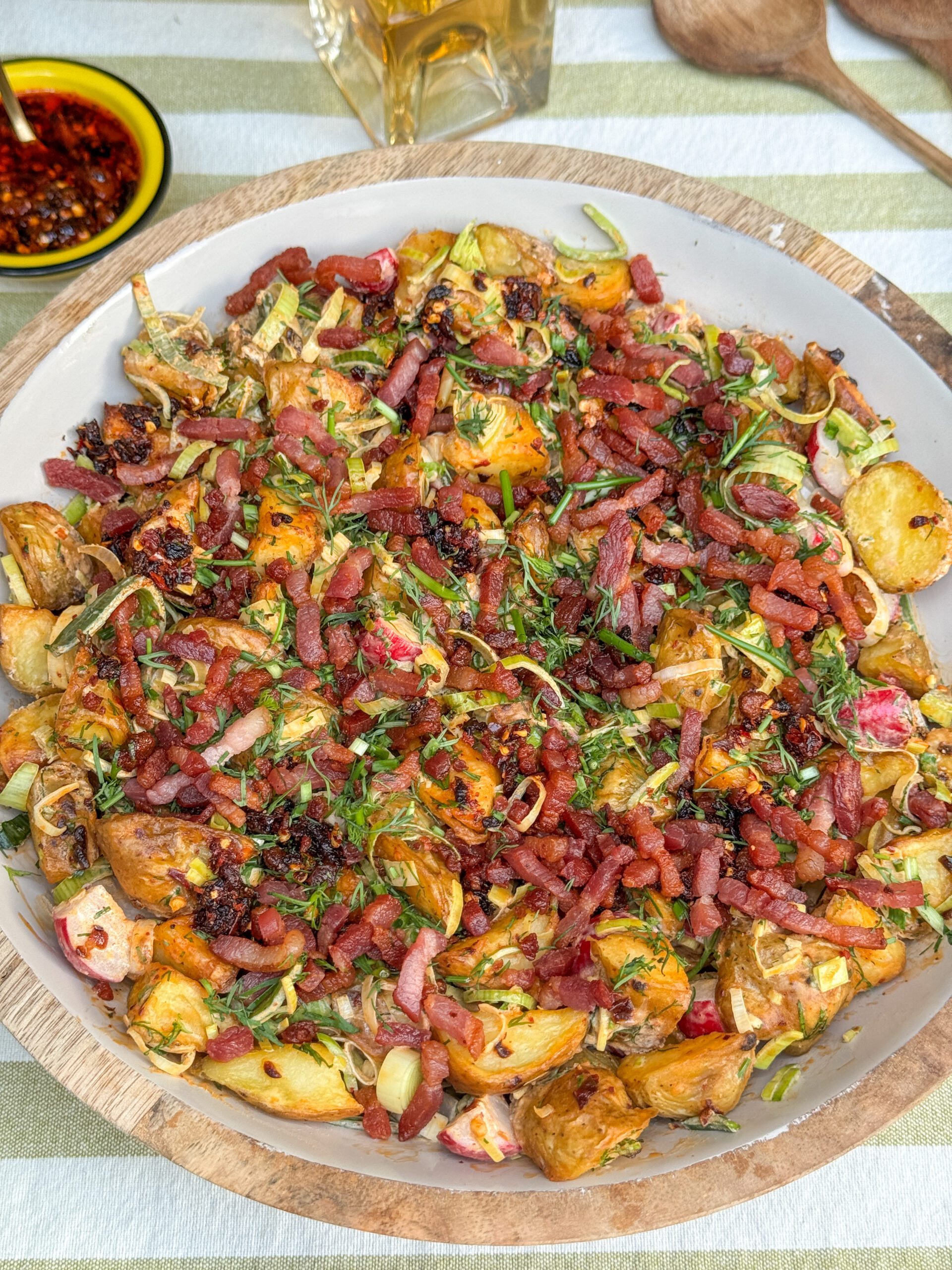krokante aardappelsalade met krokant gebakken spekjes, prei en crispy chili olie dressing in grote schaal