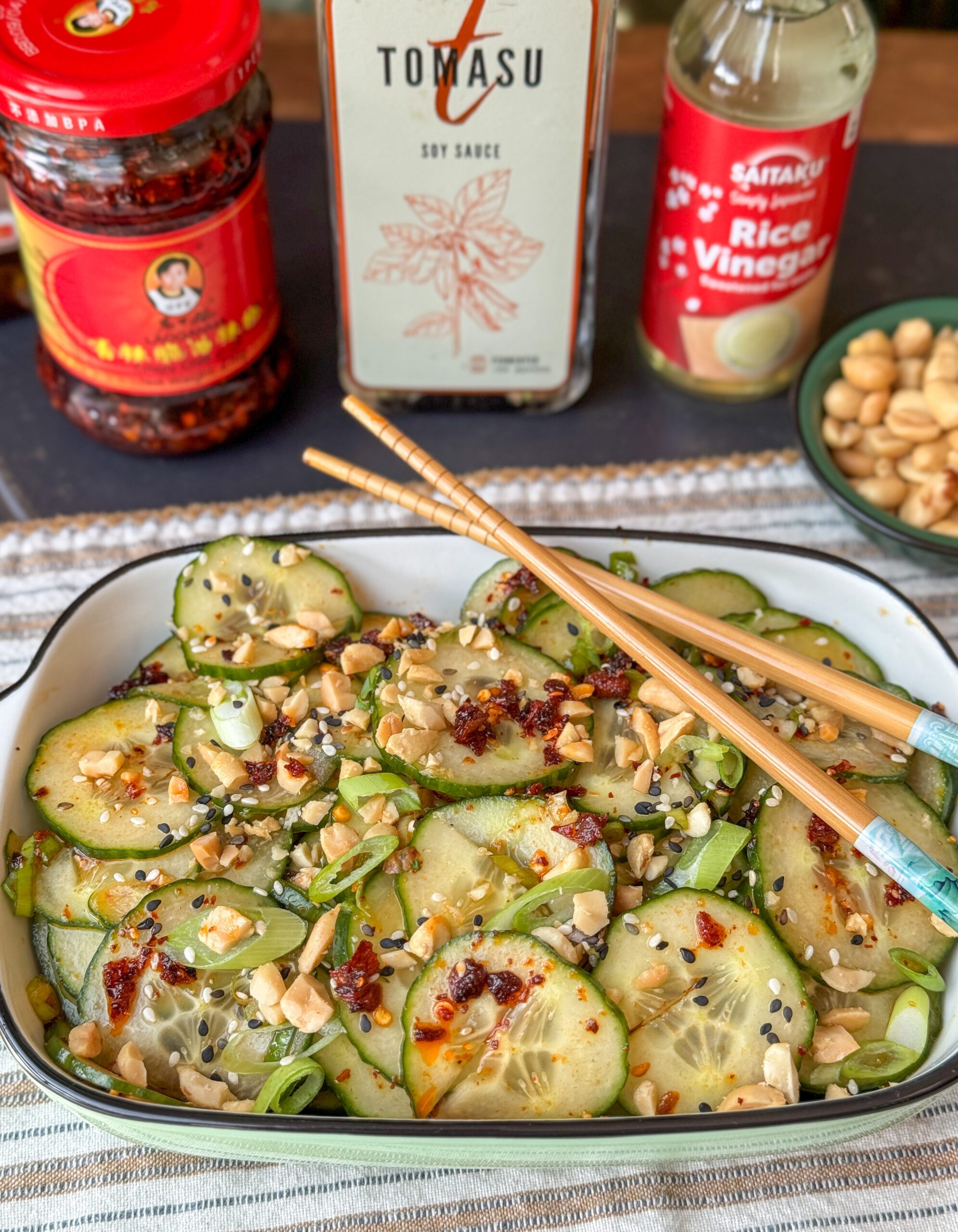 Aziatische komkommersalade - salade in wit schaaltje met pinda's, crispy chili olie, bosui, en sesamzaadjes geserveerd