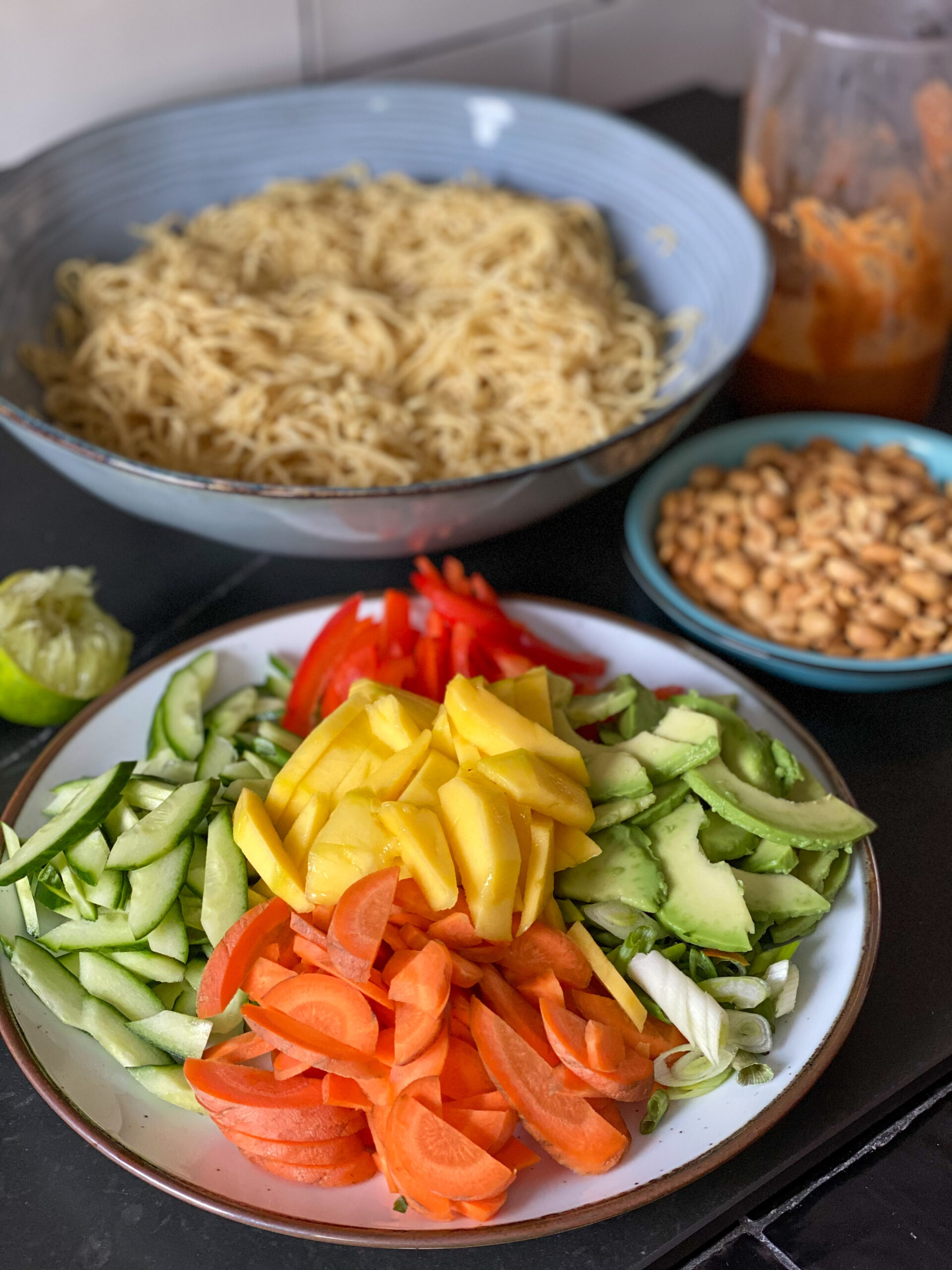 ingrediënten voor de noedelsalade met zelfgemaakte pindadressing, waaronder eiermie, mango, komkommer, paprika, avocado en wortel