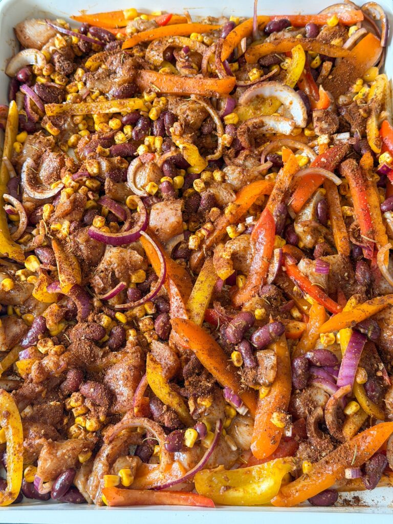 fajita traybake met kip, paprika, bonen en mais voor het bakken op de bakplaat