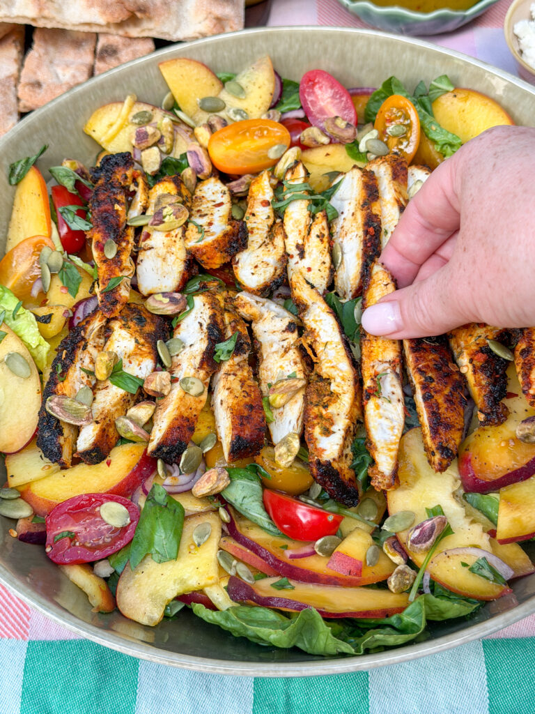 Hand pakt reepje kruidige kip van zomerse perziksalade