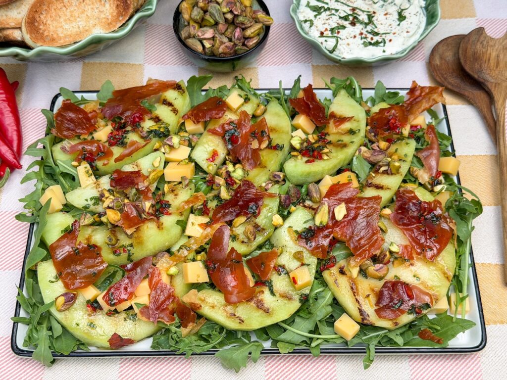 Salade met meloen en ham, gegrilde galia meloen, krokante prosciutto, blokjes kaas en pistachenoten