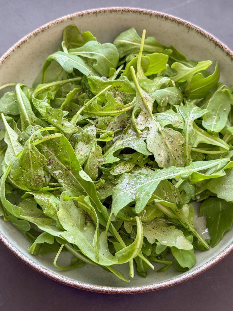 rucola op smaak brengen met olijfolie en versgemalen zwarte peper en citroensap