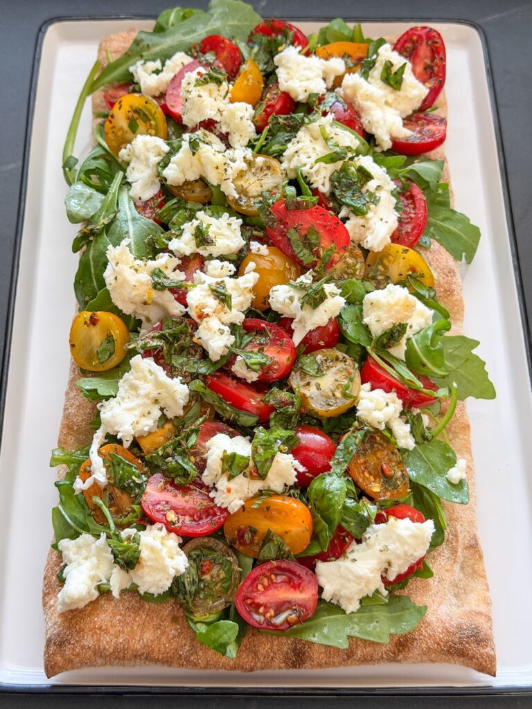 Pinsa caprese belegd met rucola, tomaten en mozzarella