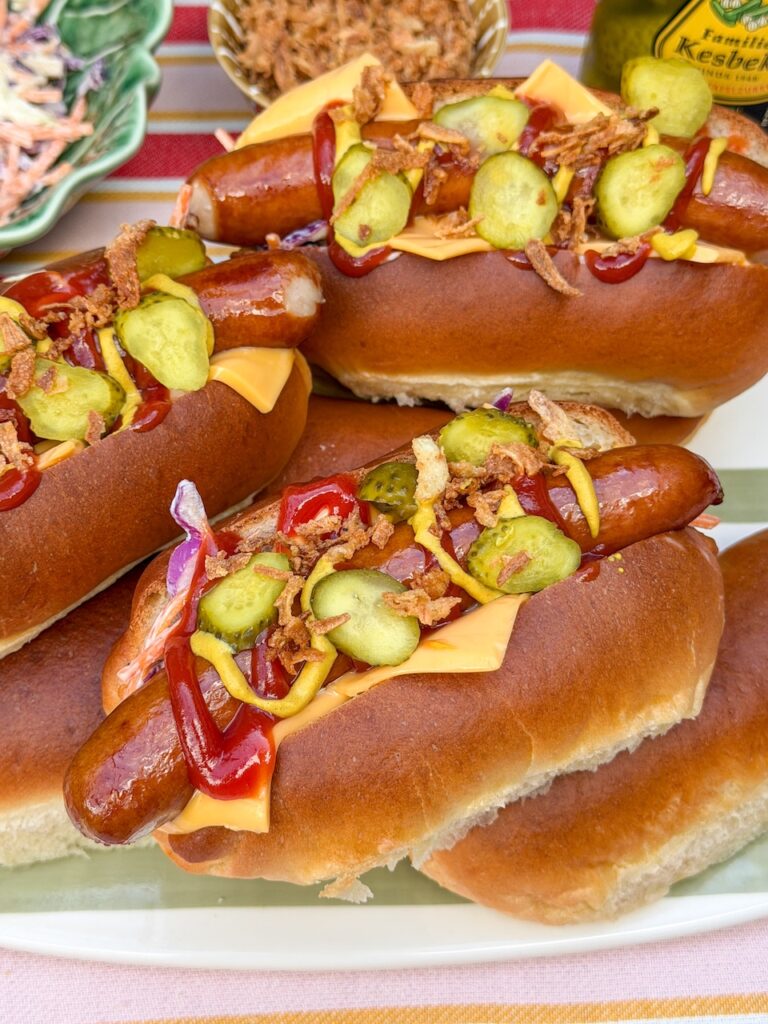 Zelfgemaakte hotdog broodjes belegd met hotdog, cheddar, coleslaw, augurk, ketchup, mosterd en gebakken uitjes