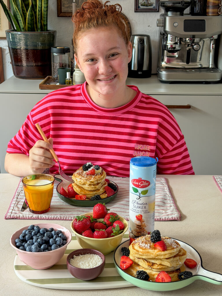 Amaranthe eet American pancakes aan eettafel geserveerd met vers fruit en poedersuiker