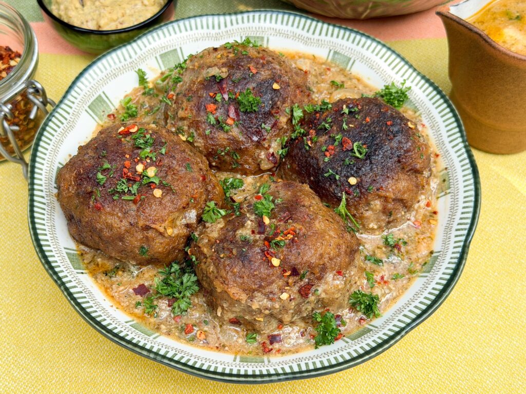 gehaktballen in mosterdjus recept met verse peterselie en chilivlokken in kom geserveerd