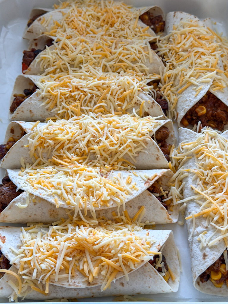 Gevulde mexicaanse wraps met gehakt en bonen bestrooid met geraspte kaas voor het bakken