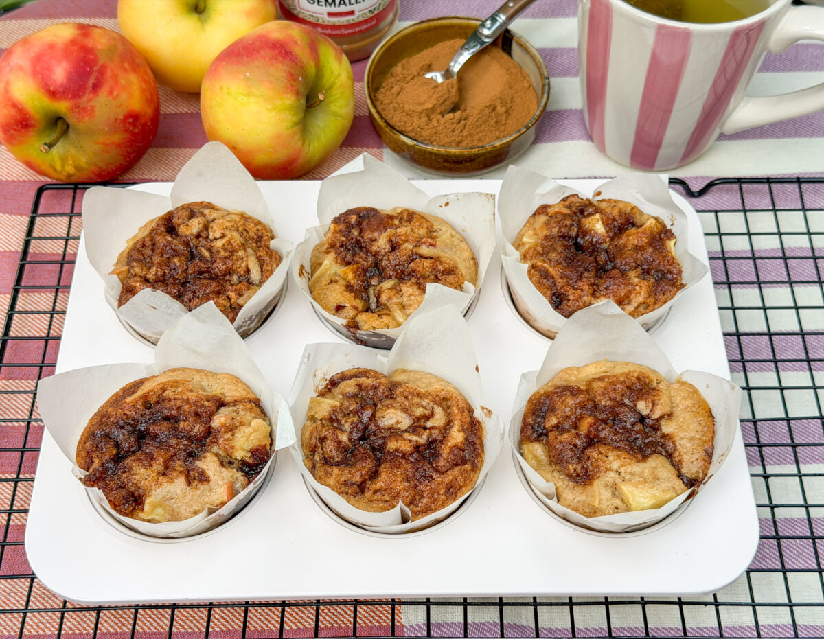 zes zelfgemaakte appel kaneel muffins met kaneelswirl, appels en kaneel op de achtergrond