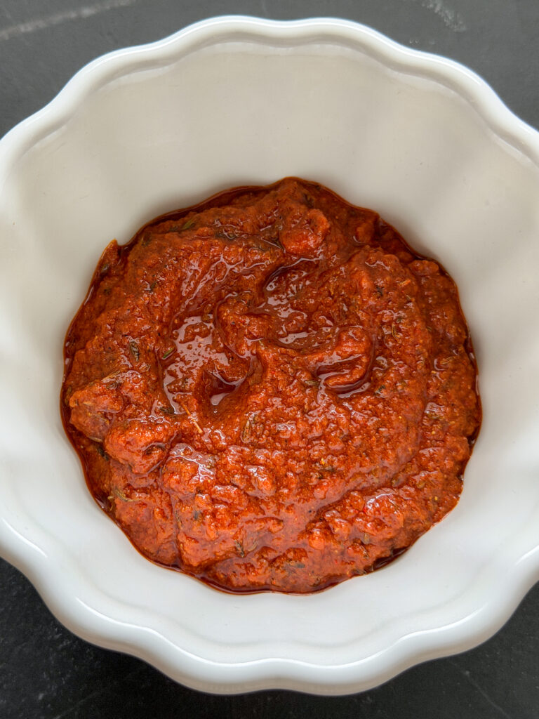 Harissamarinade met knoflook, olijfolie en specerijen in een wit schaaltje