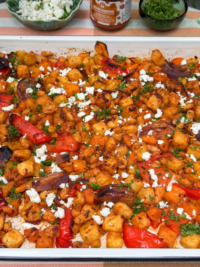 Vegetarische traybake met pompoen en krieltjes op tafel, met extra feta, peterselie en harissa erbij